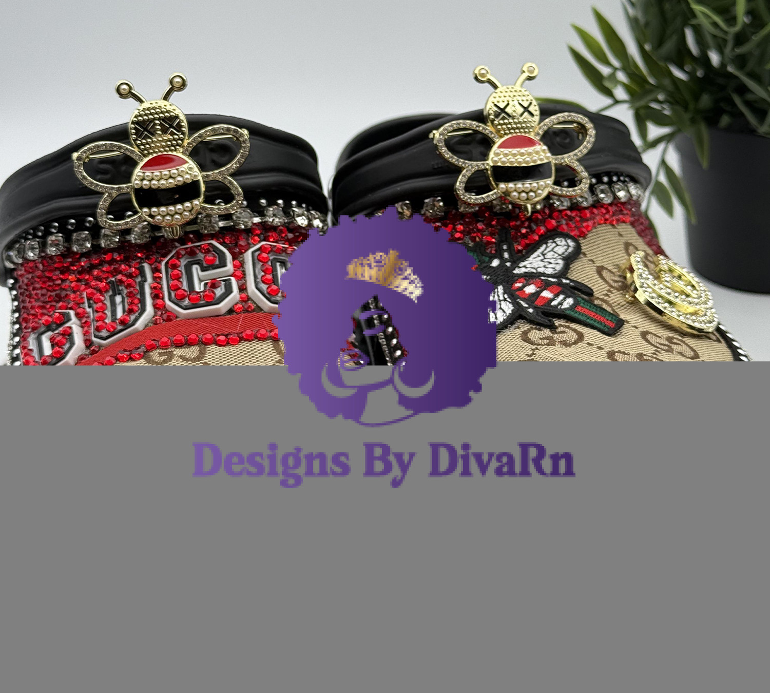 BLABEECR-023 A pair of black Crocs heavily customized in a Gucci-inspired theme, featuring red rhinestones, logo-printed fabric, and large, decorative bee charms.
