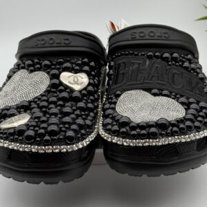 A pair of customized black Crocs, heavily embellished with black pearls, rhinestone trim, and silver rhinestone hearts.
