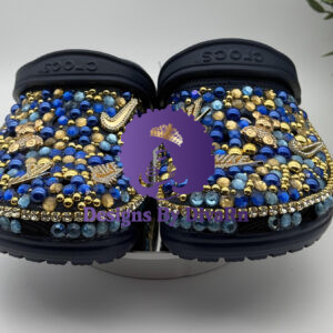 A pair of custom Decorated Blue Bead Clogs from Designs By DivaRn, featuring black clogs intricately covered in a dense mosaic of royal blue, light blue, and gold beads, and adorned with various gold rhinestone charms.
