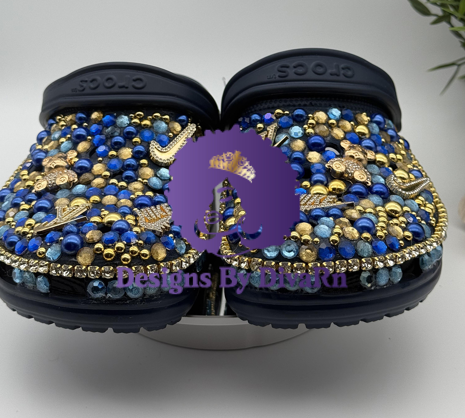 A pair of custom Decorated Blue Bead Clogs from Designs By DivaRn, featuring black clogs intricately covered in a dense mosaic of royal blue, light blue, and gold beads, and adorned with various gold rhinestone charms.