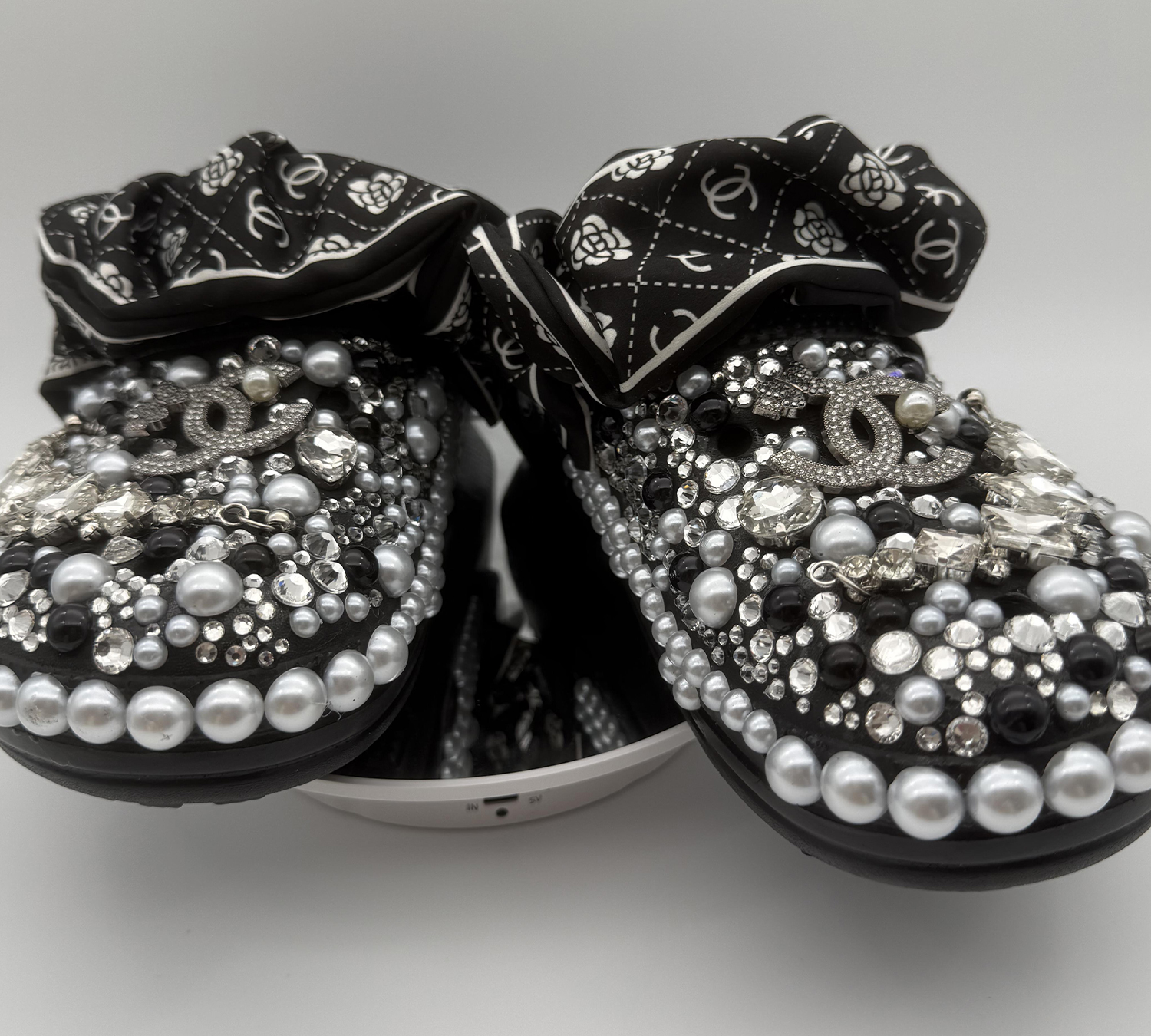 BLAEMBCR-008 A pair of black custom clogs heavily embellished with black, silver, and grey pearls, clear rhinestones, and designer-inspired charms, finished with a black and white patterned fabric strap.