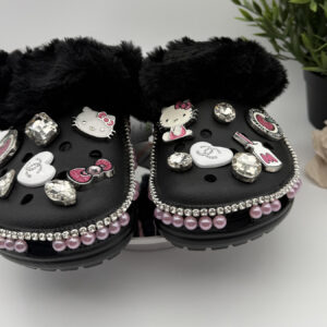 A pair of black, fur-lined clogs decorated with Hello Kitty charms, rhinestones, and pink pearls.