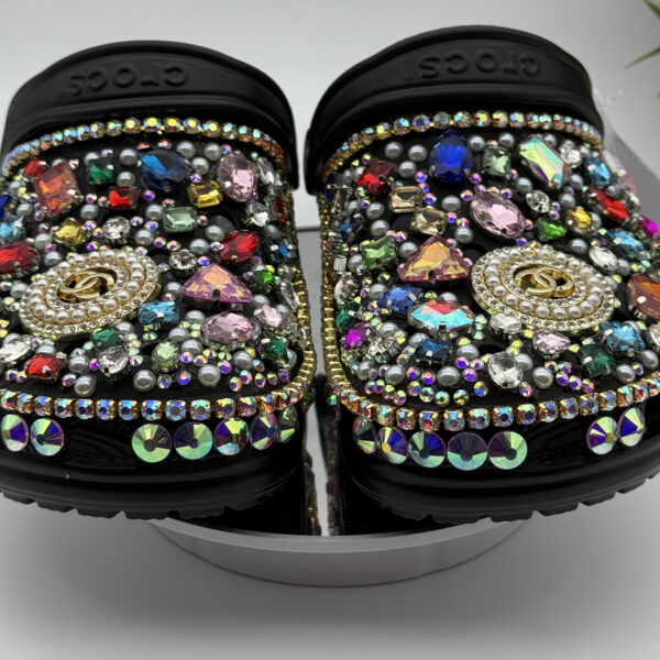 A pair of black custom Crocs heavily embellished with multi-colored rhinestones, pearls, and gold designer-inspired charms.
