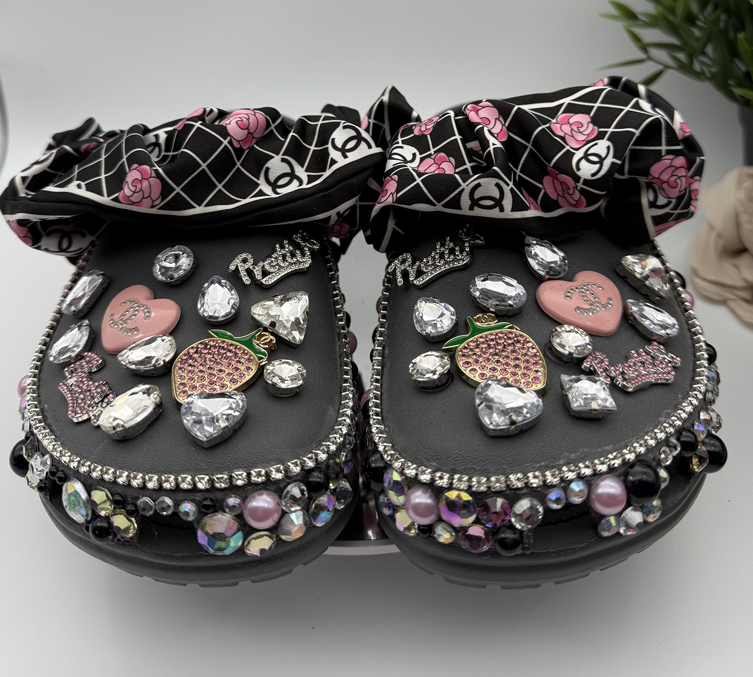 A pair of black custom clogs with a designer-inspired floral print bow strap, adorned with 