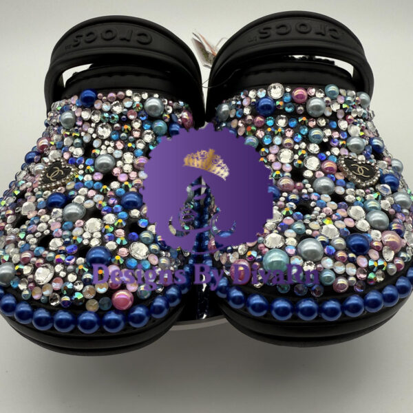 A pair of customized black Crocs, lavishly embellished with multicolored pearls and iridescent rhinestones in shades of blue and pink, and featuring Chanel-inspired charms.