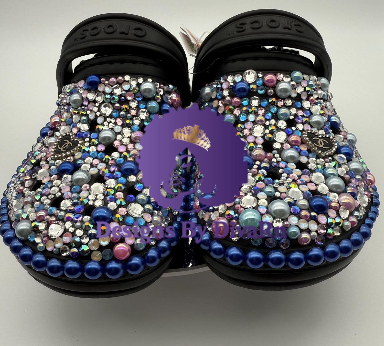 A pair of customized black Crocs, lavishly embellished with multicolored pearls and iridescent rhinestones in shades of blue and pink, and featuring Chanel-inspired charms.