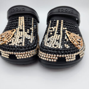 A pair of black Crocs customized with black and gold rhinestones and gold butterfly charms.