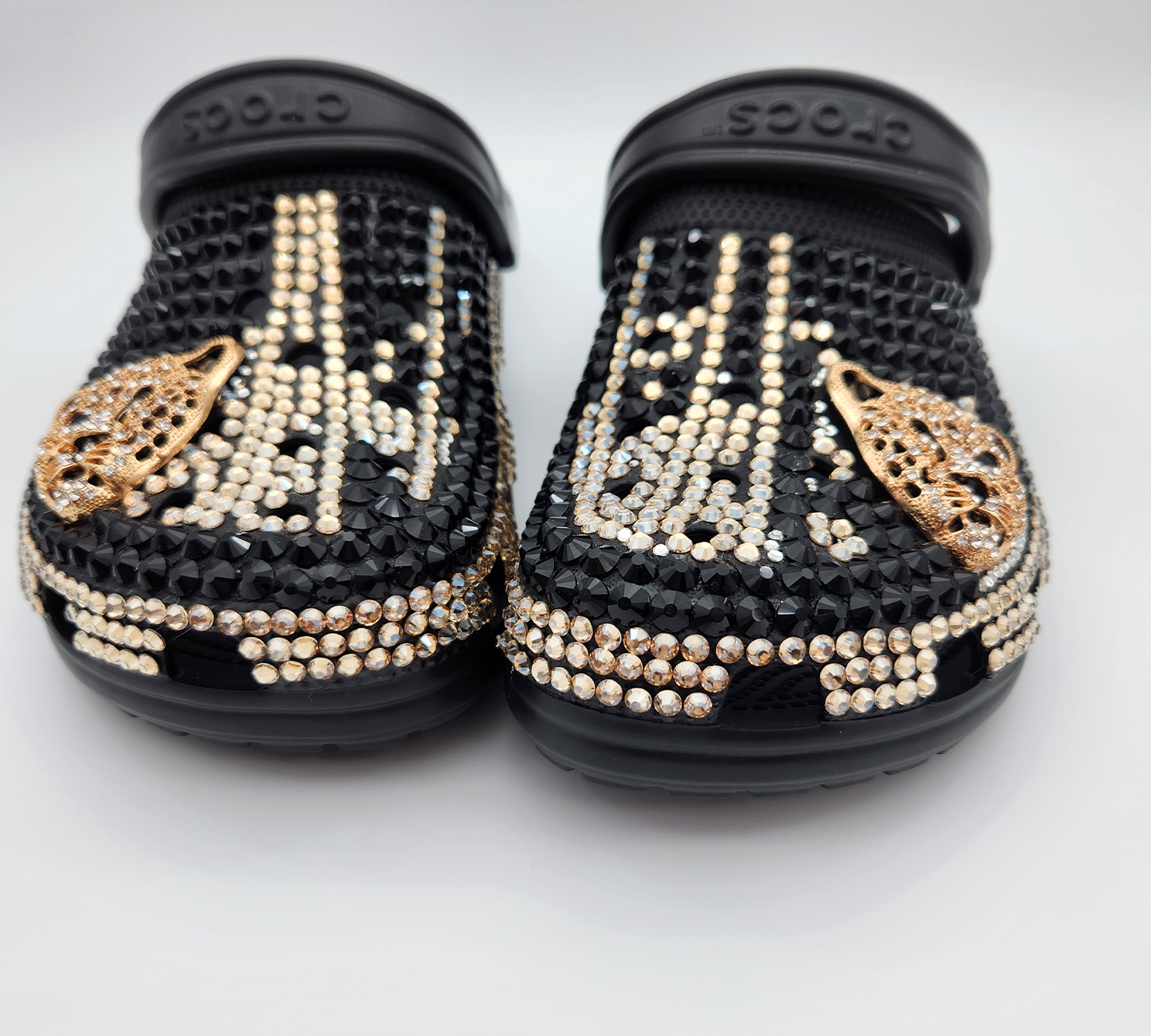 A pair of black Crocs customized with black and gold rhinestones and gold butterfly charms.