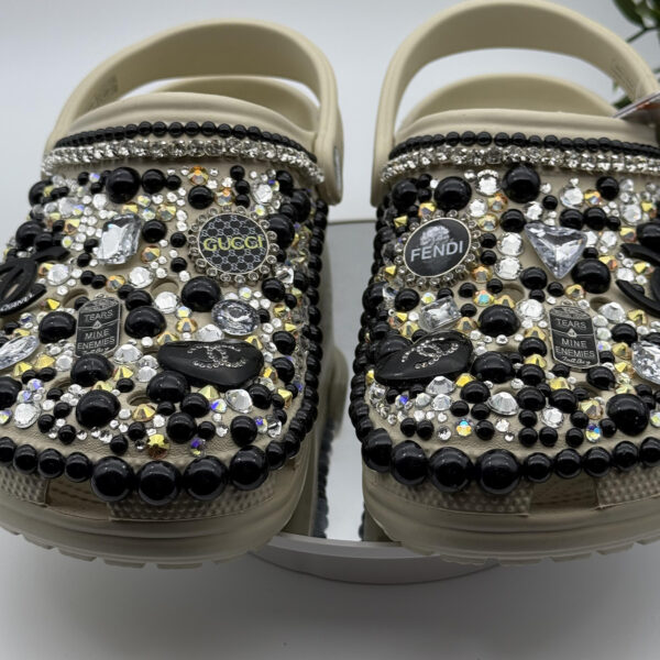 Cream-colored clogs decorated with crystals, pearls, and designer-inspired charms.