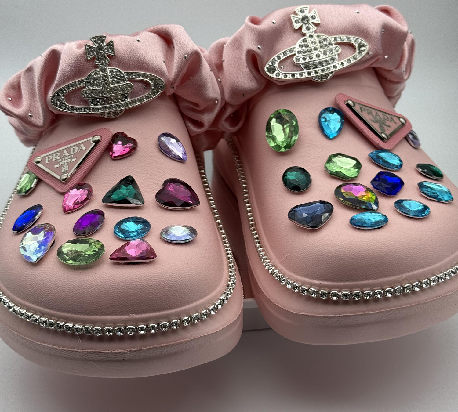 Pink clogs decorated with large, multicolored gems and a rhinestone border.