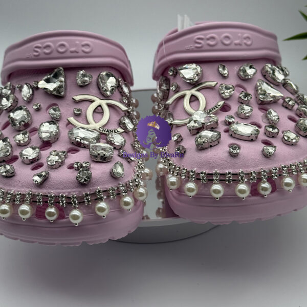 Lavender pink clogs adorned with pearls, rhinestones, and designer-inspired charms.