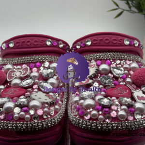 A pair of pink Bedazzled Fashion Clogs by Designs By DivaRn, heavily embellished with Hello Kitty charms, pearls, multi-colored pink and clear rhinestones, designer-inspired charms, and soft pink pom-poms, against a white background.