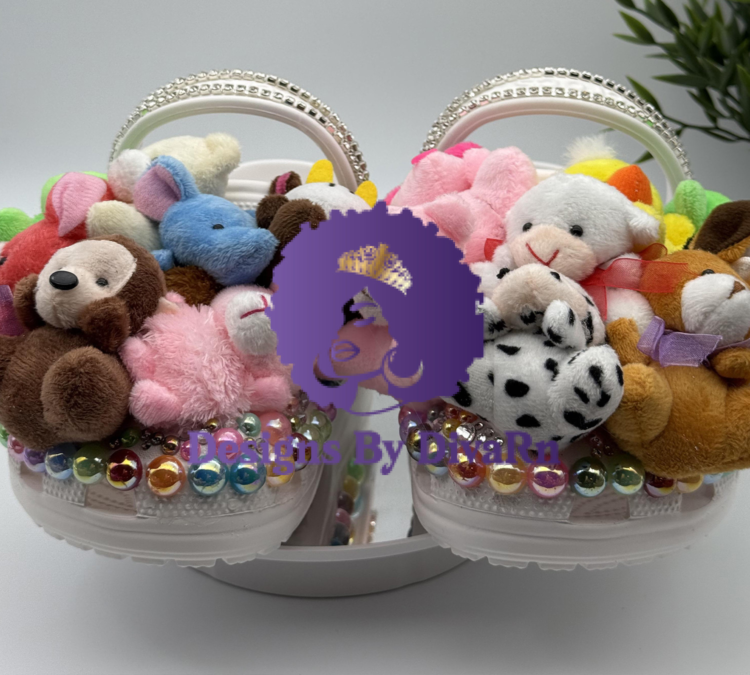 Unleash your playful side with the Cuddly Creature Clogs by Designs by DivaRN. Custom white clogs overflowing with miniature stuffed animals, iridescent gems, and a rhinestone strap.